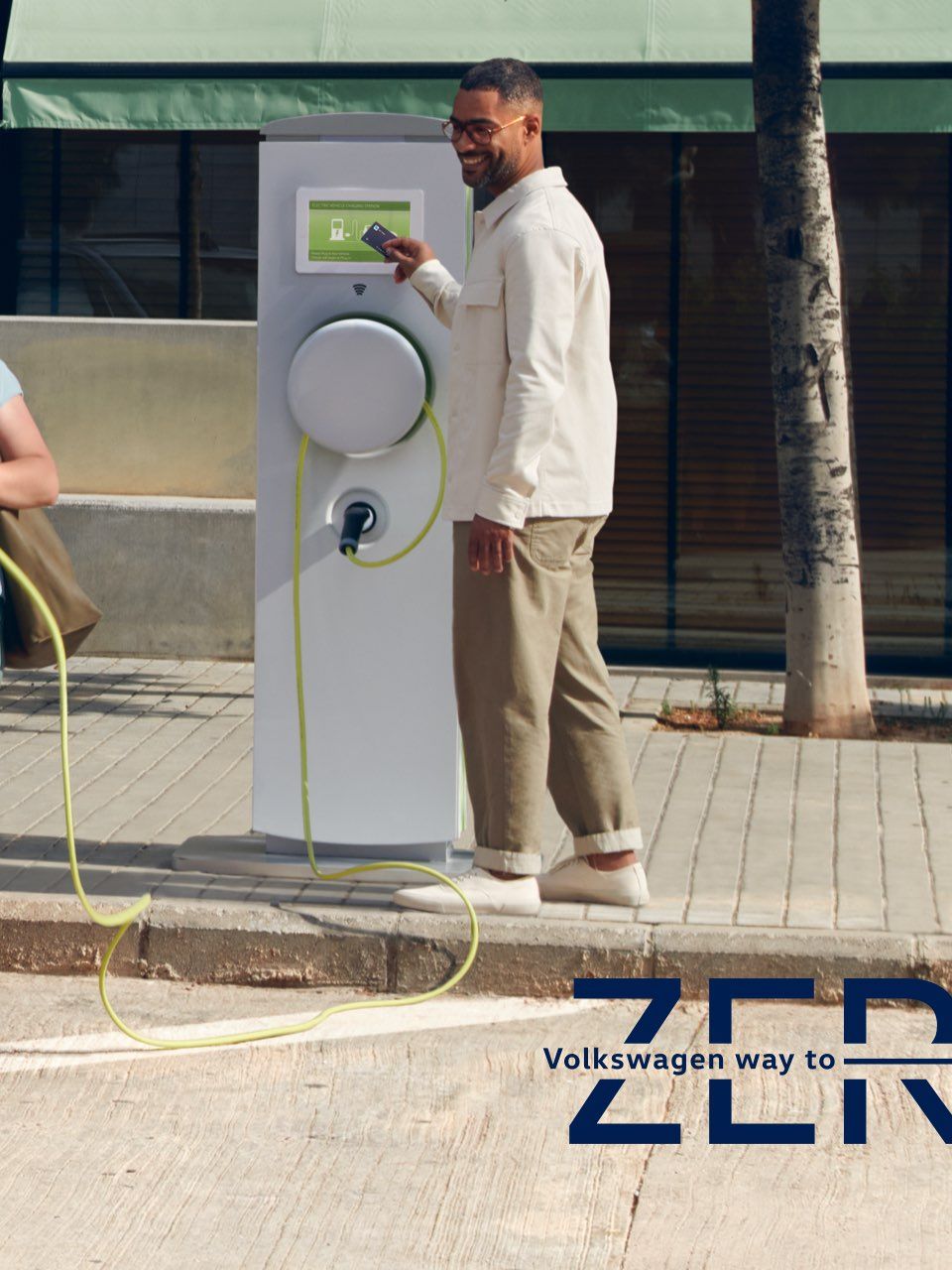 Ein Mann und eine Frau stehen an einer Ladesäule neben dem neuen VW Multivan T7 eHybrid.